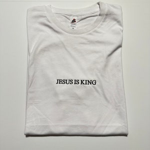 Puede incluir: Camiseta blanca con el texto "JESUS IS KING" impreso en negro en la parte delantera.