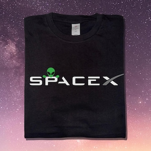 May include: Black t-shirt with the word "SPACEX" in white block letters. A green alien head graphic is above the word "SPACE". The SpaceX logo is on the right side of the text.