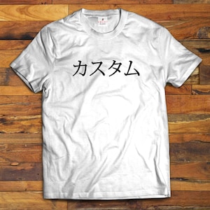 May include: A white short-sleeved t-shirt featuring the black Japanese text "カスタム" printed across the chest. The garment has a crew neckline and a small "SMART BLANKS" brand label located on the inside of the collar at the back of the neck.