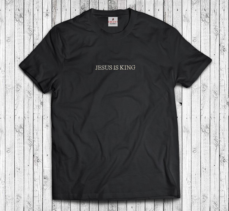 Puede incluir: Camiseta negra con el texto "JESUS IS KING" en letras doradas.