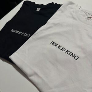 Puede incluir: Dos camisetas, una negra y una blanca, con el texto "JESUS IS KING" bordado en la parte delantera.