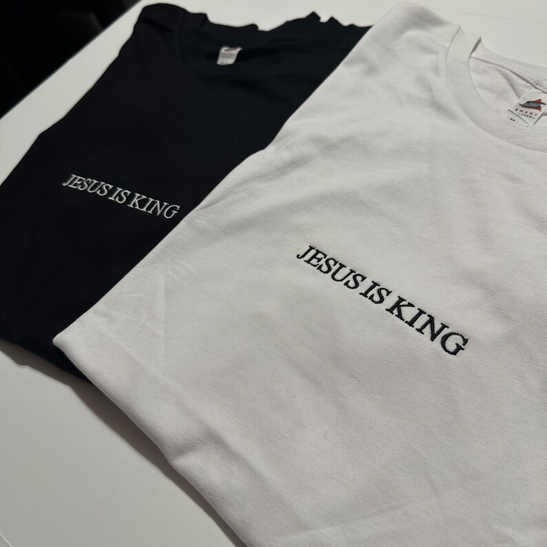 Puede incluir: Dos camisetas, una negra y una blanca, con el texto "JESUS IS KING" bordado en la parte delantera.