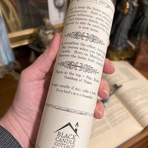 May include: White candle with a black and white label. The label says "Beautiful Nest" and includes text about the candle's use and the Roman Goddess of Peace. The bottom of the label says "Black Candle Cottage" and includes a website address.