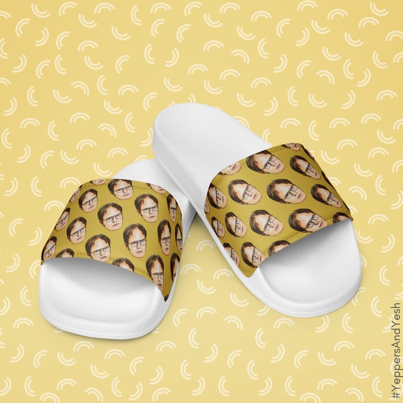 May include: White slide sandals featuring a repeating pattern of a person's face on the top strap. The face is set against a mustard yellow background. The sandals are on a yellow background with a white semi-circle pattern.