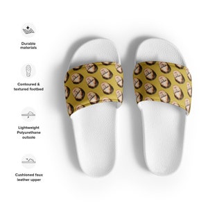 May include: White slide sandals with a yellow strap featuring a repeating pattern of a person's face. The sandals have a contoured footbed and a lightweight polyurethane outsole. The upper is made of cushioned faux leather.