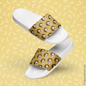 May include: White slide sandals featuring a repeating pattern of a person's face on a yellow background. The sandals have a white sole and a strap with the face pattern. The background is yellow with a white arc pattern.