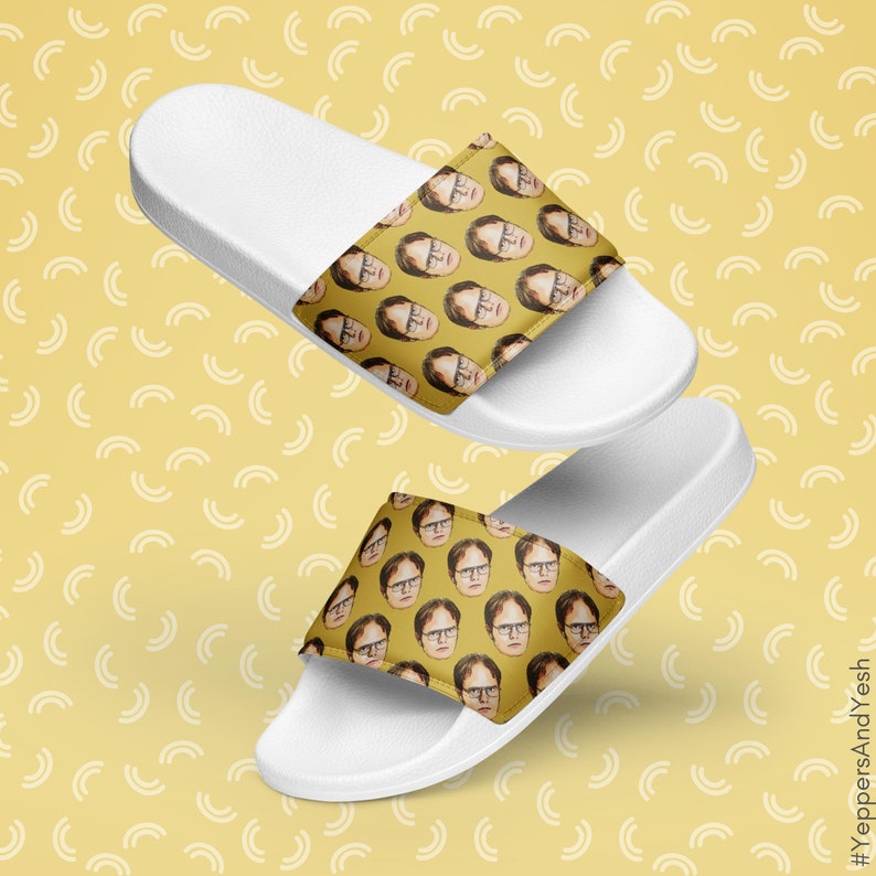 May include: White slide sandals featuring a repeating pattern of a person's face on a yellow background. The sandals have a white sole and a strap with the face pattern. The background is yellow with a white arc pattern.