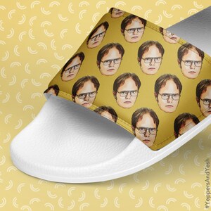 May include: White slide sandal featuring a yellow upper adorned with a repeating pattern of a man's face wearing glasses. The sandal's design is a close-up shot, showcasing the detailed print and the contrasting white sole.
