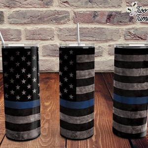 Puede incluir: Tres vasos de acero inoxidable con un diseño de bandera estadounidense desgastado y una fina línea azul. Los vasos están sobre una superficie de madera.