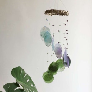 May include: A green, purple, and blue glass wind chime with a woven wood ring at the top. The chime is hanging from a white ceiling.