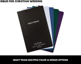 May include: A black Holy Bible with the words "Holy Bible" and "Mr. & Mrs. Brown 12.12.2023" in silver lettering. The Bible is shown with other Bibles in different colors, including white, blue, green, and purple.