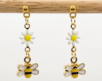 Puede incluir: Pendientes colgantes de oro con una margarita blanca y un dije de abeja amarilla y negra.