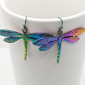 May include: A pair of iridescent dragonfly earrings with a detailed design. The earrings are made of metal and have a silver hook.