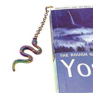 May include: A rainbow iridescent metal snake bookmark with a chain attached. The bookmark is on top of a book with the text "The Rough Guide to Yosemite" on the cover.