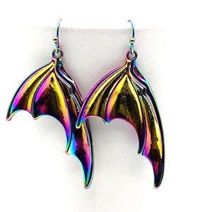 May include: A pair of iridescent dangle earrings shaped like bat wings. The metal features a metallic rainbow finish with shifting hues of purple, blue, gold, and green. Each wing is suspended from a simple metal hook for pierced ears.