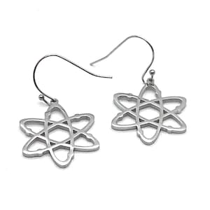 May include: A pair of silver-colored atom-shaped dangle earrings. Each earring features a six-pointed star design with intersecting lines, suspended from a simple hook. The earrings are made of a shiny, metallic material.