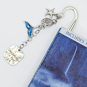May include: Silver bookmark with a blue mermaid tail charm, a starfish, a seashell, and a tag that says "Dreaming of the Sea".