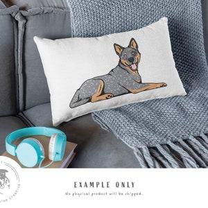 May include: A white throw pillow with a cartoon illustration of a blue heeler dog lying down. The dog has a blue and white speckled coat and is looking to the right. The pillow is on a gray couch with a gray throw blanket.