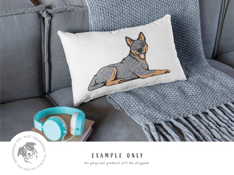 May include: A white throw pillow with a cartoon illustration of a blue heeler dog lying down. The dog has a blue and white speckled coat and is looking to the right. The pillow is on a gray couch with a gray throw blanket.