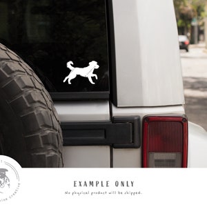 May include: White silhouette of a dog running on a silver car. The car has a black tire and a red taillight. The text "est. 2021 the canine creative" is in a circle on the lower left corner of the image.