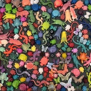 Peut inclure: Une collection d'ornements en plastique colorés représentant des animaux et des insectes. L'assortiment comprend des tortues, des lézards, des papillons et des ours de différentes couleurs comme le vert, l'orange et le violet. Certains ont de petits cercles noirs.