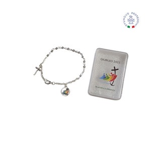 Pode incluir: Pulseira de prata com uma cruz e um amuleto com uma imagem colorida de um barco com pessoas nele. A pulseira vem em uma caixa de plástico transparente com o texto "Giubileo 2025" e "Pellegrini di Speranza".