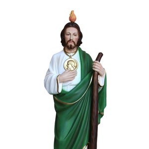 May include: A detailed statue of a religious figure, featuring a white robe with gold trim, a green cloak, and a wooden staff. The figure has a beard, a halo, and a medallion. The statue stands on a dark brown base.