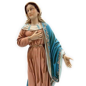 May include: A figurine of the Virgin Mary, standing with her hands clasped in prayer. She is wearing a blue robe with gold trim and a white head covering. The figurine is standing on a black base.