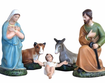 May include: A traditional nativity scene with a ceramic baby Jesus, Mary, Joseph, a cow, and a donkey. The figures are painted in realistic colors and are arranged in a circle around the baby Jesus.