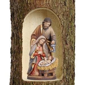Può includere: Un presepe in legno con una rappresentazione scolpita della Sacra Famiglia. Le figure sono dipinte in toni caldi e sono inserite all'interno di un tronco d'albero cavo.
