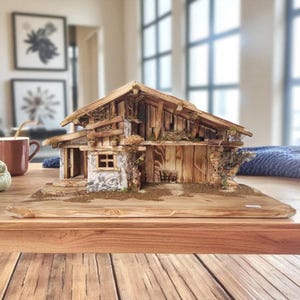 Può includere: Una casa in miniatura rustica in legno con tetto spiovente, piccola finestra e porta in legno. La casa è realizzata con vari pezzi di legno e ha un aspetto naturale e invecchiato. Poggia su una base di legno ed è decorata con piccole piante.