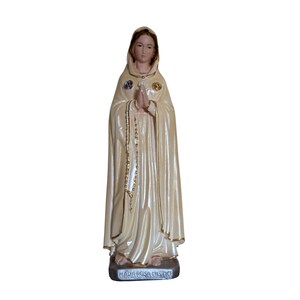 Peut inclure: Statue cr&egrave;me d'une figure religieuse, les mains jointes en pri&egrave;re. La figure porte une cape &agrave; capuche avec des bordures dor&eacute;es et un chapelet. La base de la statue porte l'inscription "MARIA ROSA MISTICA".