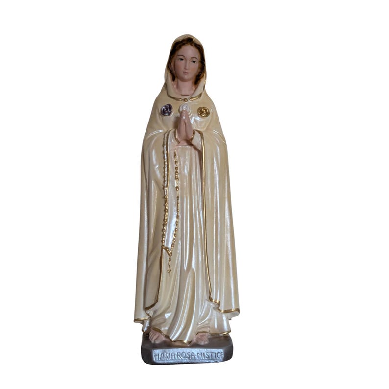 Peut inclure: Statue cr&egrave;me d'une figure religieuse, les mains jointes en pri&egrave;re. La figure porte une cape &agrave; capuche avec des bordures dor&eacute;es et un chapelet. La base de la statue porte l'inscription "MARIA ROSA MISTICA".