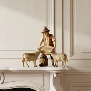 Op de afbeelding: Een handgesneden houten beeldje van een herder met een bruine hoed, vest en broek, die een gevlochten ovale mand vasthoudt. De herder staat tussen twee lichtbruine schapen met gedetailleerde wolstructuur op een vlakke ondergrond.
