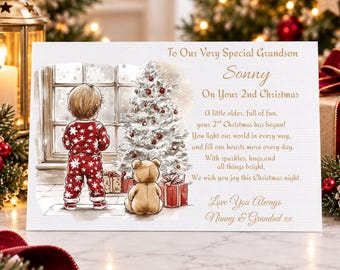 May include: A rectangular greeting card featuring a child in red snowflake pajamas and a teddy bear standing before a decorated Christmas tree. The text reads: To Our Very Special Grandson Sonny On Your 2nd Christmas, followed by a poem and Love You Always Nanny & Grandad xx.