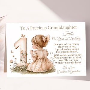 以下が含まれることがあります： 「To A Precious Granddaughter Indie On Your 1st Birthday」と書かれたバースデーカード。女の子のイラスト、大きな数字の1、蝶、花が描かれています。カードには詩が添えられ、「Grandma & Grandad」と署名されています。