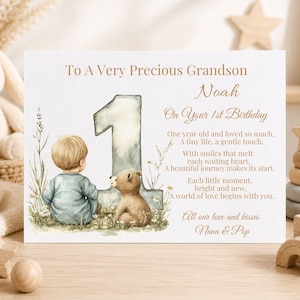 May include: A white rectangular greeting card featuring a watercolor illustration of a child and a teddy bear sitting next to a large number one. The text reads: To A Very Precious Grandson Noah On Your 1st Birthday, followed by a poem and All our love and kisses Nana & Pop.