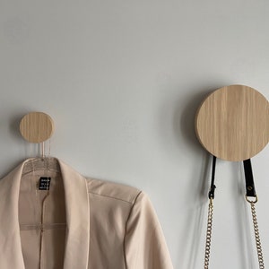 May include: Two wooden wall hooks, one larger than the other, with a gold chain hanging from the larger hook. The smaller hook has a beige blazer hanging from it.