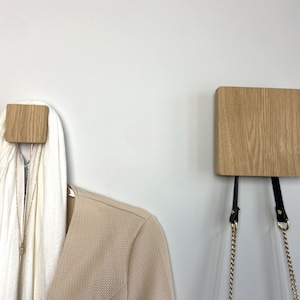 May include: Two wooden wall hooks with a white scarf hanging on one. The hooks are made of light wood and have a simple, modern design.