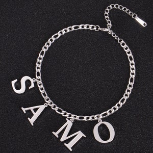Può includere: Collana a catena d'argento con quattro ciondoli a forma di lettera che compongono la parola "SAMO".