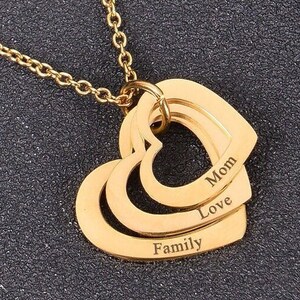 Puede incluir: Collar de oro con un colgante de corazón en capas grabado con las palabras "Mamá", "Amor" y "Familia".