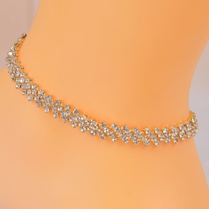 May include: A gold chain with a double row of clear rhinestones, arranged in a zig-zag pattern.