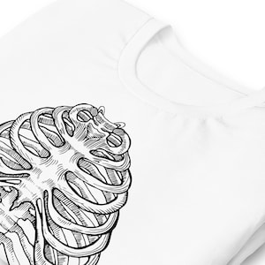 Może przedstawiać: Biała koszulka z czarno-białą ilustracją klatki piersiowej. Grafika znajduje się z przodu koszulki, widoczny jest kołnierz i ramię. Projekt to szczeg&oacute;łowy rysunek anatomiczny.