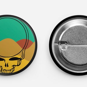 May include: A round button with a black border and a colorful graphic of a skull with a yellow, green, and brown background. The skull is surrounded by a circle with a yellow sun and a green sky.