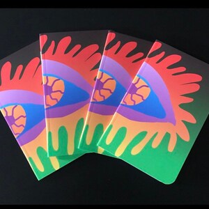May include: Four colorful notebooks with a psychedelic eye design. The notebooks have a black background with a gradient to green. The eye design is in shades of red, orange, yellow, green, blue, purple, and pink.
