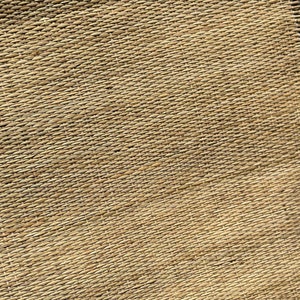 May include: A close-up of a woven natural fiber mat with a light brown color. The mat has a rough texture and is made of thin, tightly woven strands. The mat is slightly frayed at the edges. The text 'Jassy Artcraft' is visible in the bottom right corner of the mat.