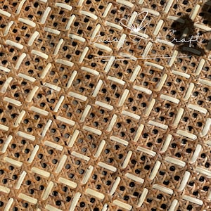 Pode incluir: Close-up de um material de rattan tecido com um padrão geométrico repetitivo. O rattan de tom natural é entrelaçado com tiras de cor mais clara, criando uma superfície texturizada. O design apresenta pequenas aberturas circulares escuras.