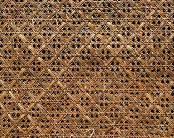 Pode incluir: Close-up de um material de rattan tecido com um padrão geométrico repetitivo. O material de tons naturais apresenta um design em forma de diamante, com pequenos orifícios escuros nas interseções da trama. O texto "Jassy Art Craft" está escrito em itálico branco.