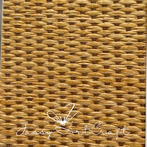 May include: Close-up of a woven material with a repeating pattern of light brown and dark brown fibers. The texture is intricate, with each fiber interlaced to create a basket-like design. The text "Jassy Art Craft" is written in cursive.
