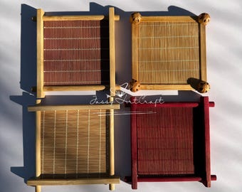 May include: Four square bamboo coasters in shades of brown and red. Each coaster has a rectangular frame with a woven bamboo mat insert. Two coasters have decorative wooden accents at the corners.